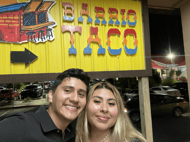 Steven and Susie taking a picture in front of the barrio taco sign